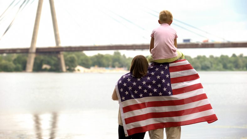 Back view of family wrapped in USA flag looking at bridge, independence day