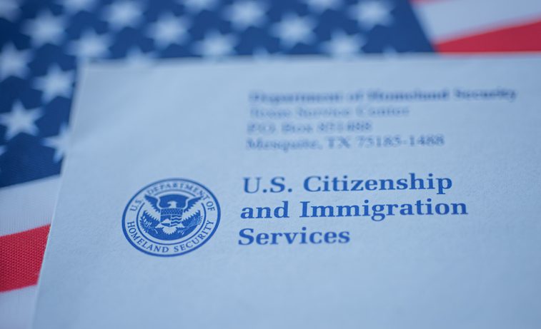Hand touching Letter (Envelope) from USCIS on  flag of USA background.